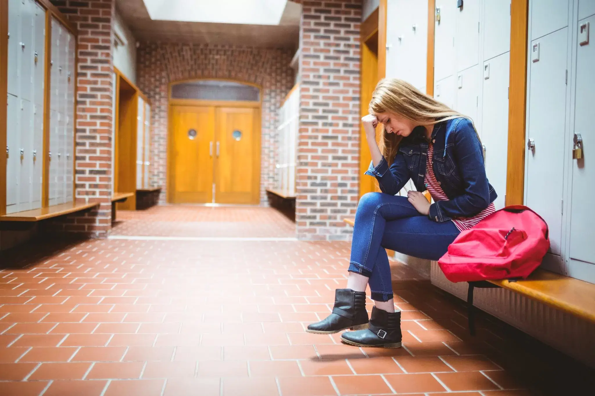 teenage girl sitting on a bench at school, looking worried and anxious