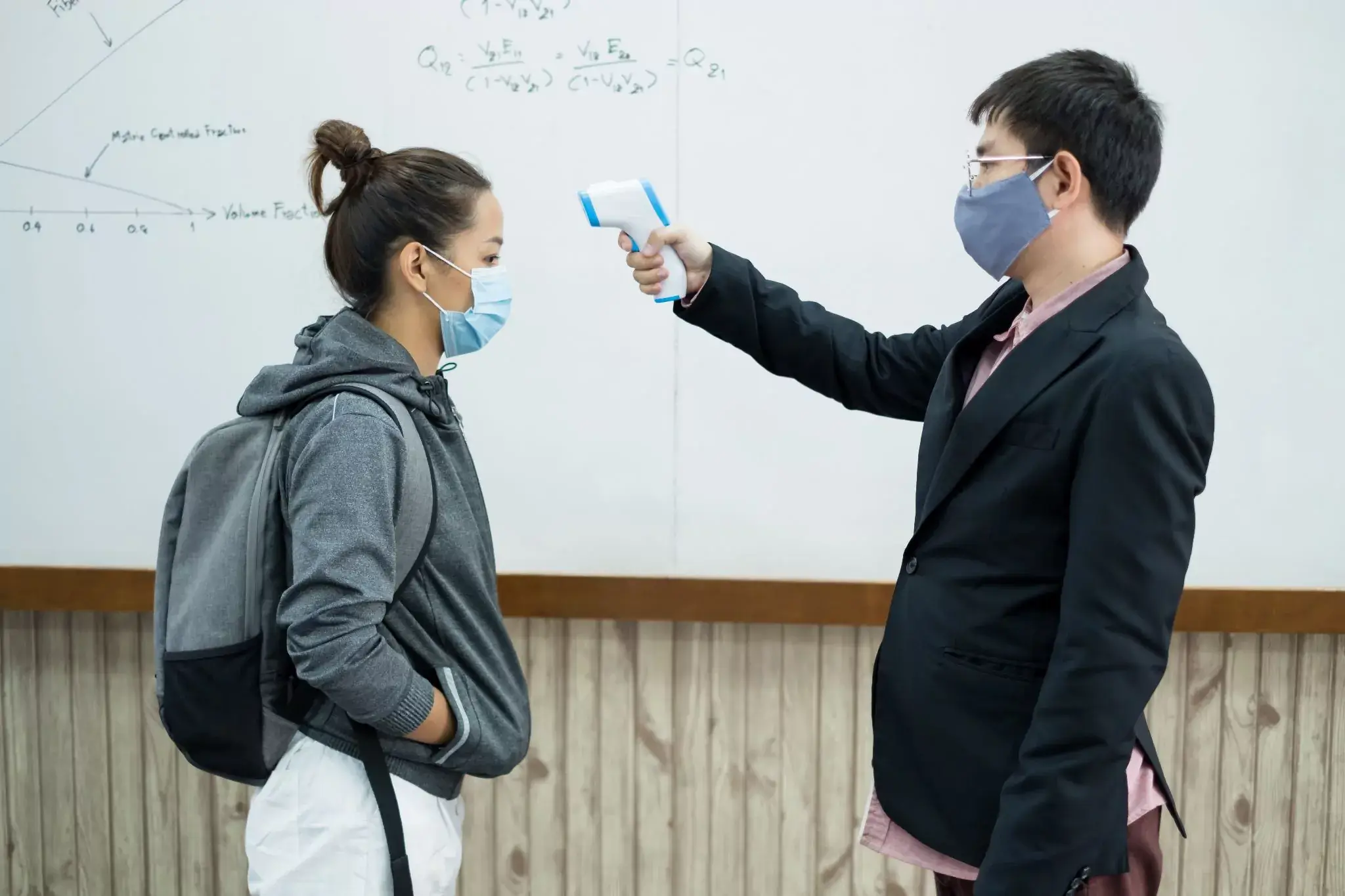 teenager getting temperature measured in classroom, wearing mask to prevent Covid-19