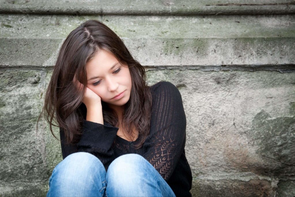 eenage girl sitting against a wall looking depressed