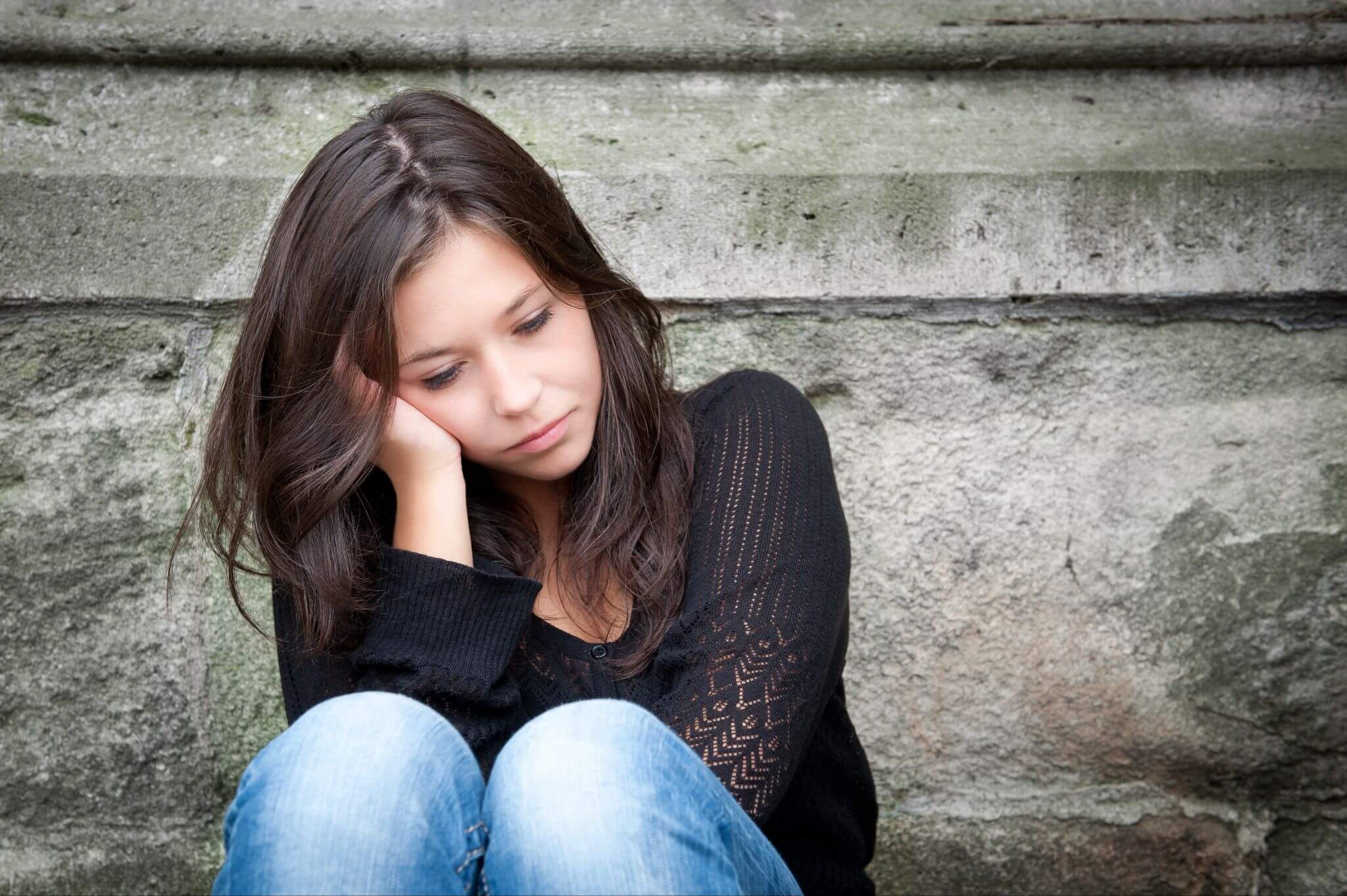 eenage girl sitting against a wall looking depressed