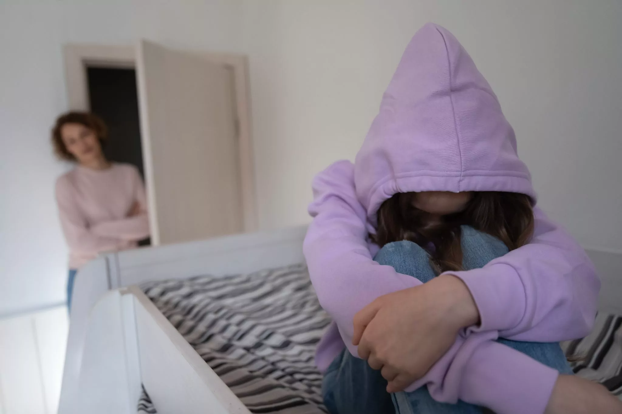 teenager wearing her hood low over her face, hiding from mother in background